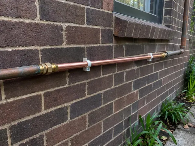 Repaired copper water pipe fixed along a brick exterior wall in Northbridge