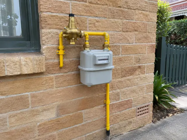 Outdoor gas meter with new yellow fittings on a brick house wall in Northbridge
