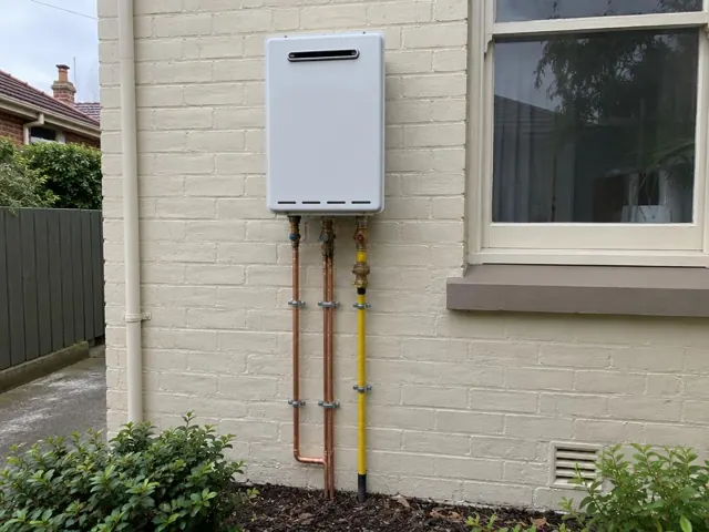 Wall-mounted hot water unit with copper and gas pipes on a painted brick exterior in Cremorne